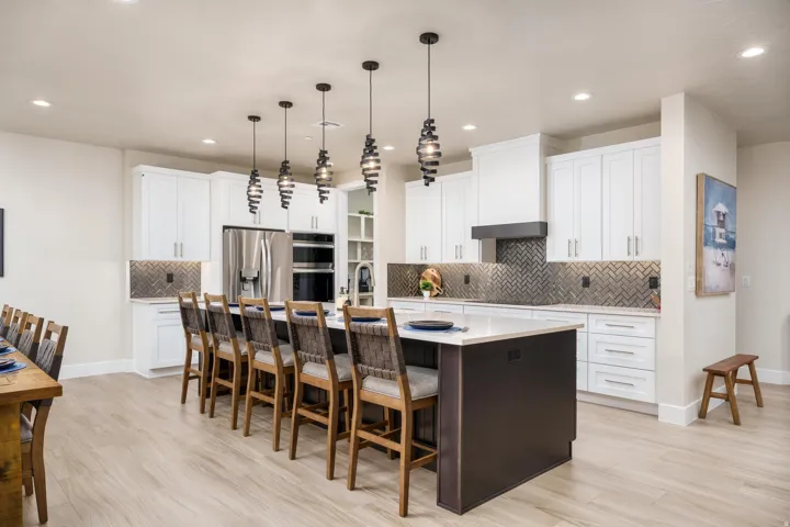 Kitchen featuring white cabinetry, stainless steel appliances, a dark herringbone backsplash, a central island with seating, and pendant lighting