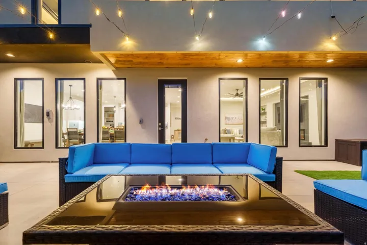 Expansive outdoor patio featuring a built-in fire pit, multiple dark-framed windows and doors, and a wood-panel ceiling accent
