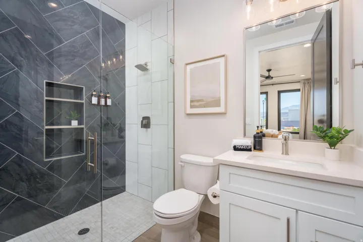 Glass-enclosed shower with dark tile surround and built-in shelving, white vanity with integrated sink, chrome faucet, and rectangular mirror
