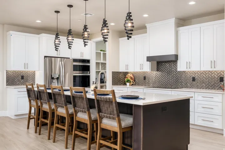 Gourmet kitchen with stainless steel appliances, herringbone tile backsplash, white shaker cabinetry, and a large island featuring pendant lighting