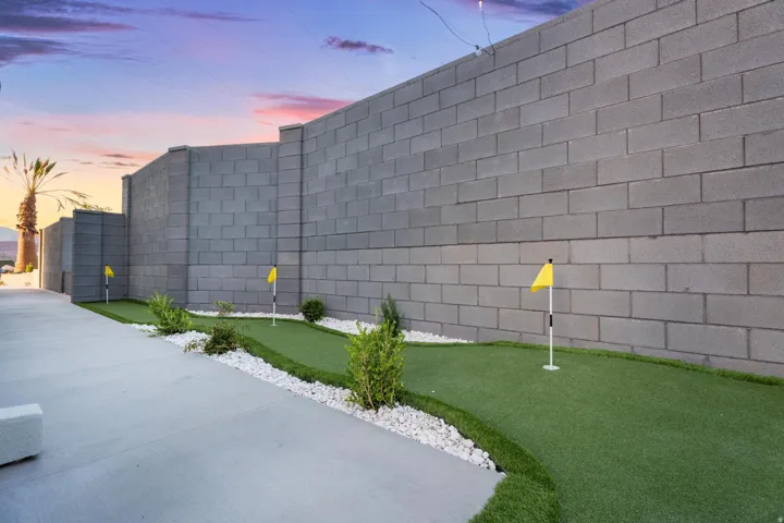 Putting green with artificial turf, bordered by white gravel and low-maintenance plantings