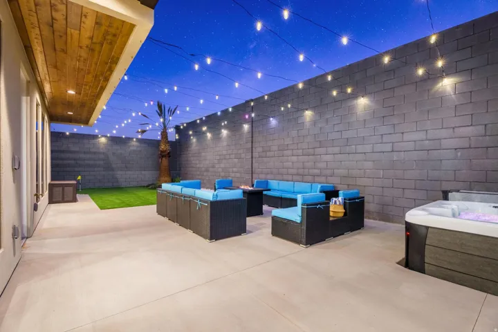 Private outdoor living area featuring a hot tub, string lighting, and an artificial turf lawn