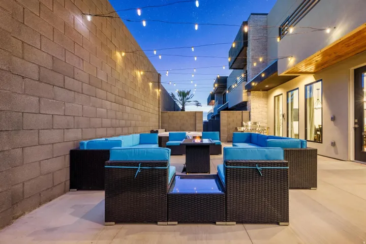 Expansive outdoor patio with string lighting, built-in outdoor kitchen, concrete block privacy walls, and multiple large windows