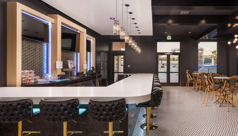 Extended bar counter with integrated seating, pendant lighting, geometric tile flooring, and multiple sets of glass double doors