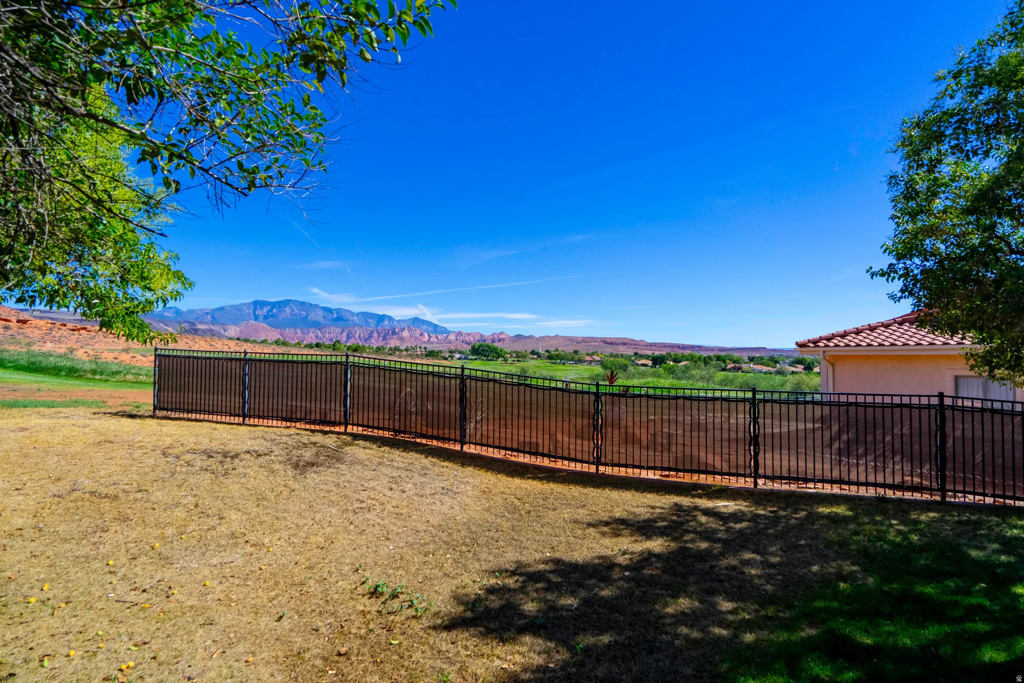 Expansive outdoor space featuring a black metal fence, mature trees, and distant mountain scenery