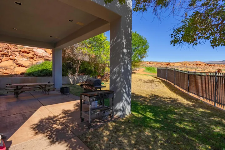 Covered patio with concrete flooring, recessed lighting, and an adjacent grassy area with a black metal fence