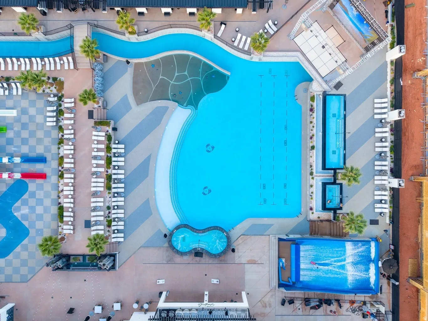 Expansive aquatic facility featuring a large swimming pool, a meandering lazy river, a dedicated lap pool, and a surf simulator