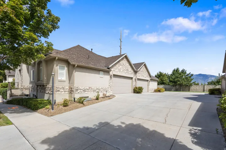 Stucco and stone facade with multiple garage doors, a concrete driveway, and a paved sidewalk
