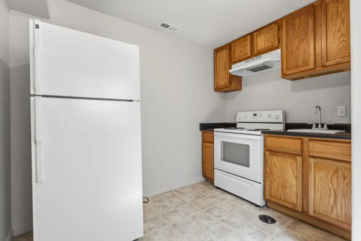 Kitchen featuring wood cabinetry, dark countertops, a white top-freezer refrigerator, a white electric range, and a stainless steel sink with a chrome faucet