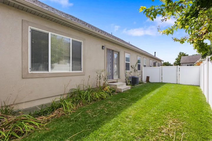 Expansive fenced yard featuring a manicured lawn, stucco exterior, and a sliding glass door