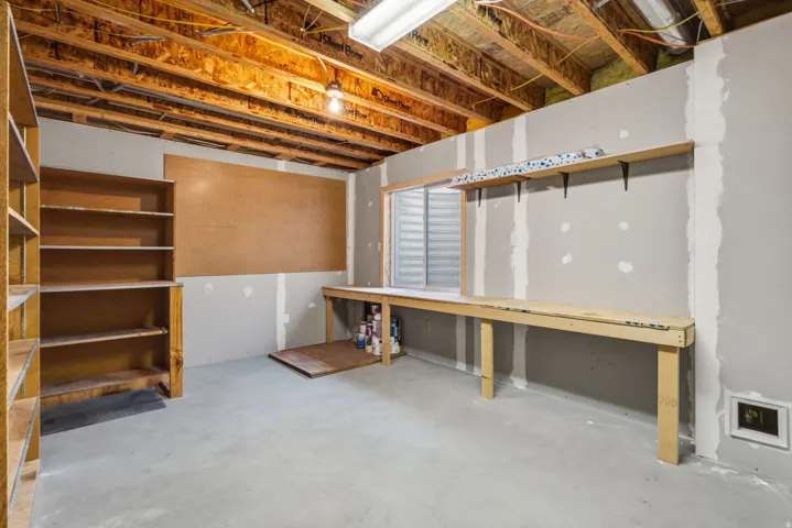 Unfinished space featuring a concrete floor, exposed ceiling joists, built-in shelving, a built-in workbench, and overhead lighting
