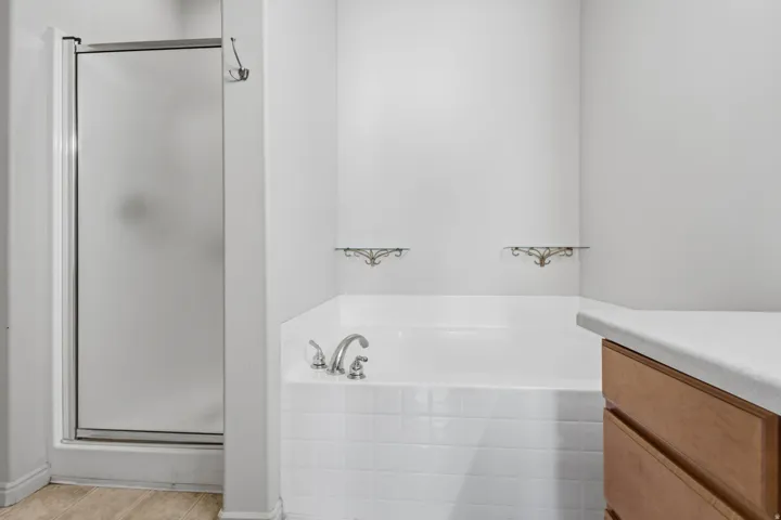 Built-in soaking tub with white tile surround, adjacent to a shower with a frosted glass enclosure