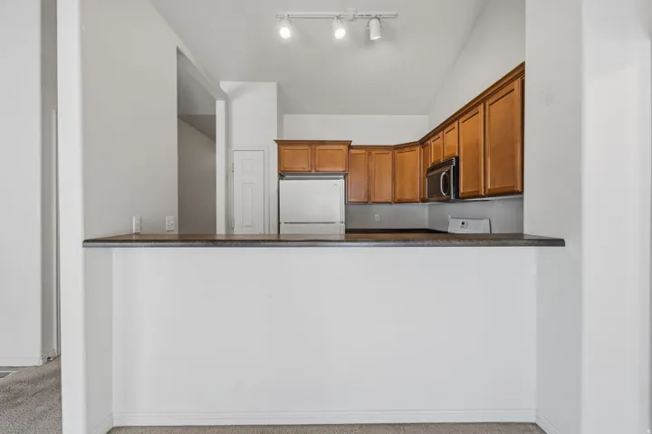 Kitchen featuring wood cabinetry, dark countertops, stainless steel refrigerator, and built-in microwave