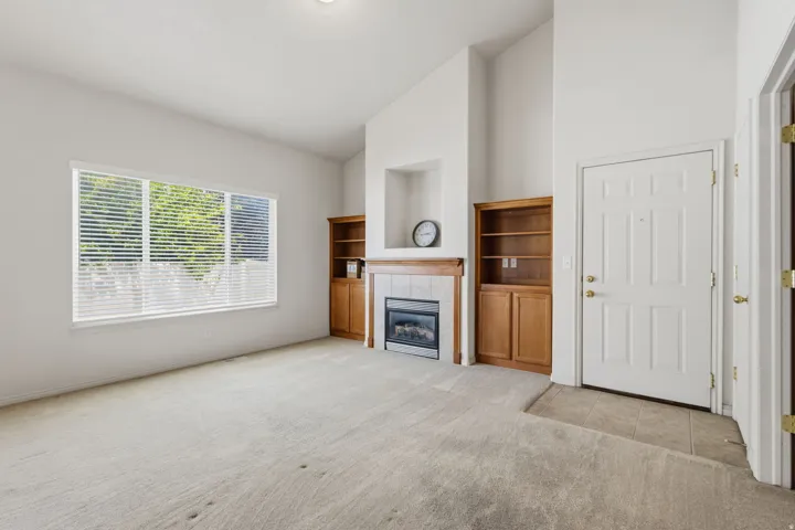 Vaulted ceilings, carpeted flooring, built-in shelving, tile fireplace surround, and recessed wall niche