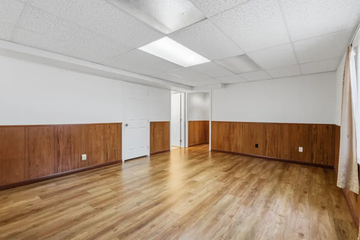 Wood-finish flooring, drop ceiling, wood paneling, recessed lighting, and white walls