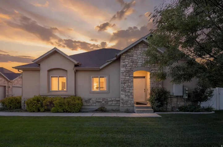 Stucco exterior with stone accents, architectural shingle roof, and a mature tree