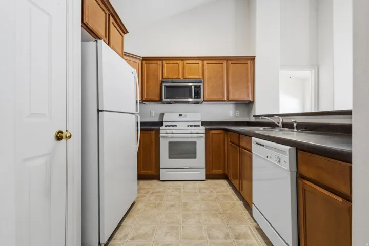 Kitchen featuring wood-finish cabinetry, white appliances, and a vaulted ceiling