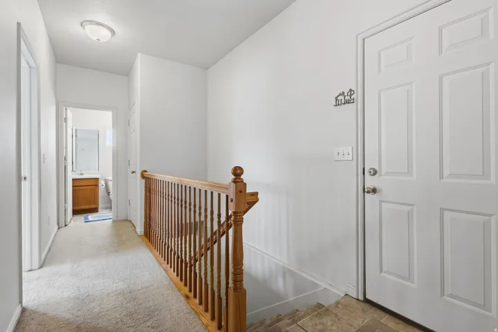 Wood-finish staircase with turned wood newel post and balusters, accompanied by a white paneled door and overhead flush-mount lighting