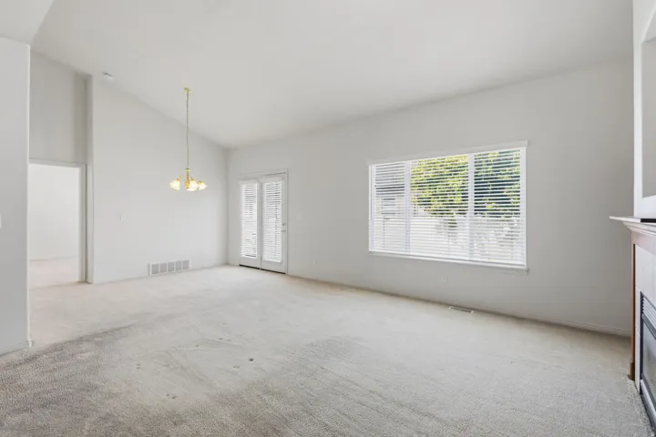 Vaulted ceiling, ceiling-mounted light fixture, carpeted flooring, double French doors, and a fireplace with a wood mantel