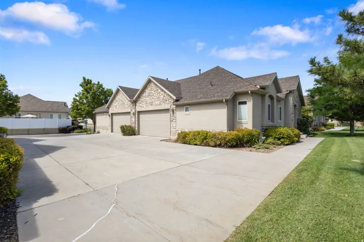 Stucco exterior with stone accents, multiple garage doors, a concrete driveway, a sidewalk, and landscaped shrubbery