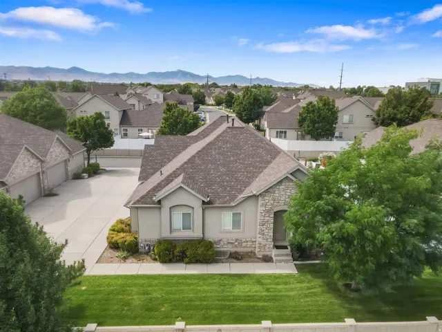 Stone and stucco exterior with a composite shingle roof, featuring a concrete driveway and mature landscaping