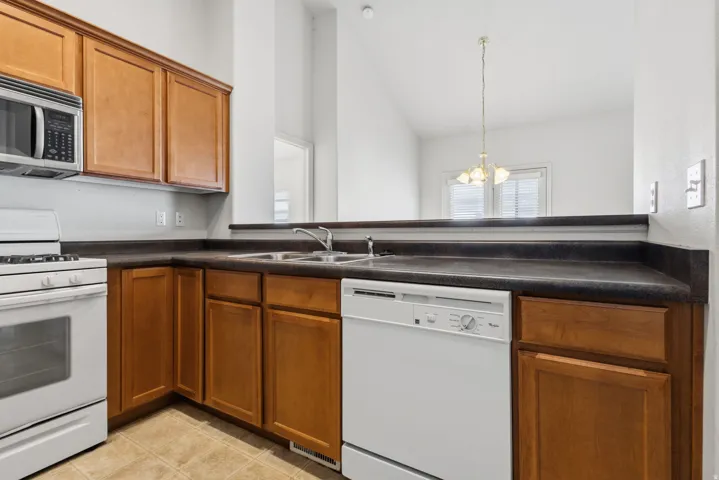 Kitchen featuring wood-finish cabinetry, dark countertops, a stainless steel microwave, and white appliances