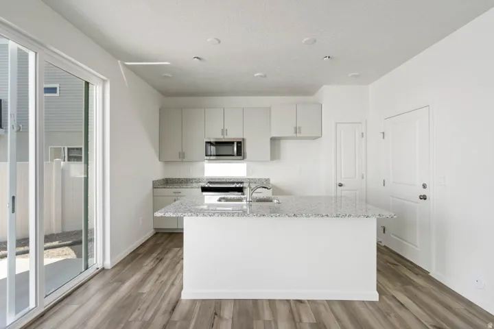 Kitchen featuring a central island with a built-in sink, stainless steel appliances, light gray cabinetry, and wood-finish flooring