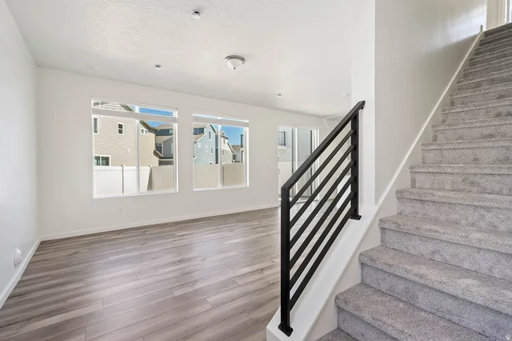 Wood-finish flooring, multiple windows, built-in ceiling lighting, carpeted staircase with modern black railing, and white walls