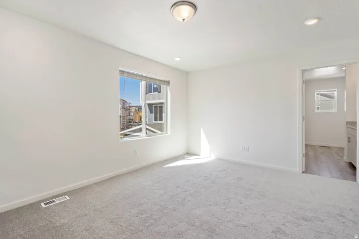 Bright room with light gray carpeting, a large window, a ceiling-mounted light fixture, recessed lighting, and white wall finishes