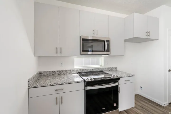 Modern kitchen featuring white cabinetry, granite countertops, stainless steel microwave, and wood-finish flooring
