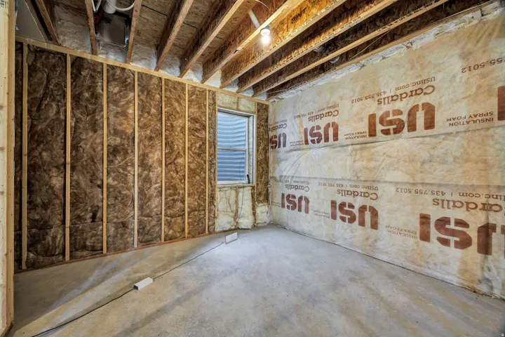 Unfinished basement space featuring exposed wood framing, concrete flooring, and a single window
