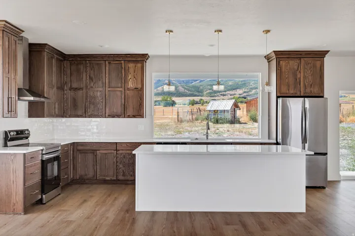 Spacious kitchen featuring wood-finish cabinetry, stainless steel appliances, a white subway tile backsplash, and an expansive window with a mountain backdrop
