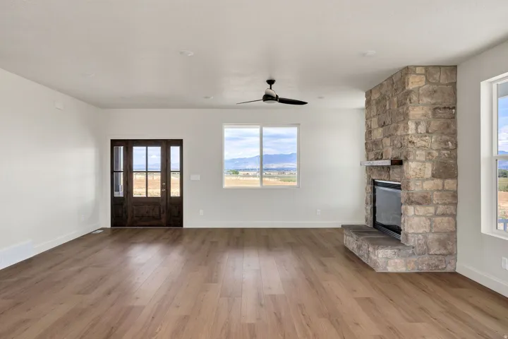 Spacious room with wood-finish flooring, a stone fireplace, and multiple windows