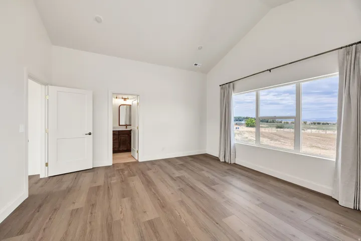 Vaulted ceiling, wood-finish flooring, white paneled doors, large window with expansive outdoor scenery, and recessed lighting