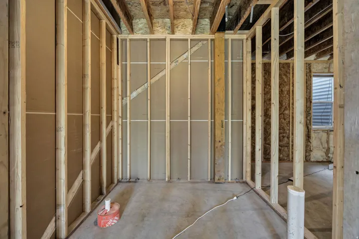 Unfinished interior framing with exposed ceiling joists, concrete flooring, and an egress window