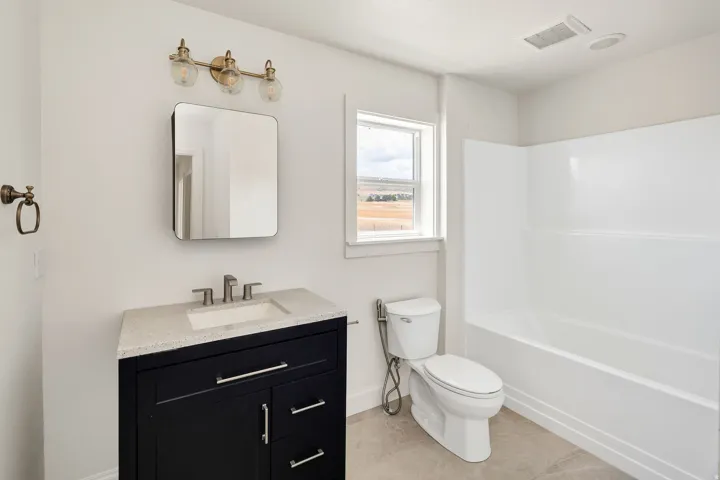 White tub/shower combination, dark wood-finish vanity with light countertop, rectangular undermount sink, brushed nickel faucet, and a rectangular framed mirror