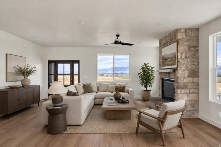 Virtually staged. Spacious living area featuring wood-finish flooring, a stone-clad fireplace with a hearth, and abundant natural light