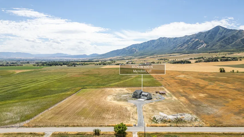 Expansive property featuring a modern gray-sided residence, a detached auxiliary structure, and a gravel driveway