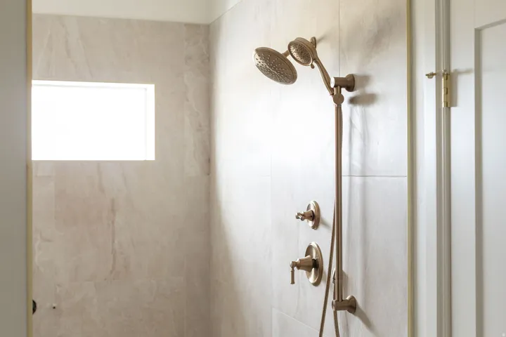 Tiled shower with a fixed and handheld showerhead, individual control handles, and an integrated window