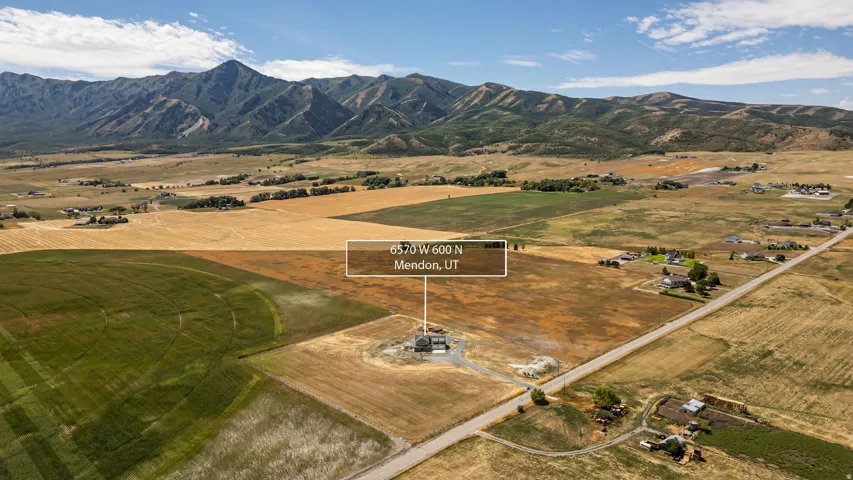 Expansive land parcel with surrounding agricultural fields, mountainous backdrop, and a paved road