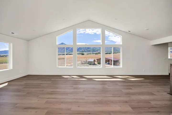 Vaulted ceiling, wood-finish flooring, expansive window array, recessed lighting, and white wall finishes