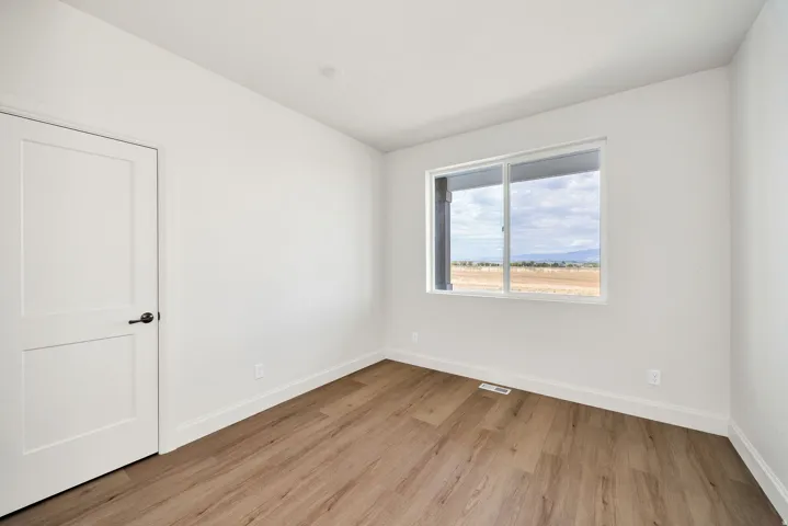 Wood-finish flooring, white walls, and a white two-panel door with black hardware