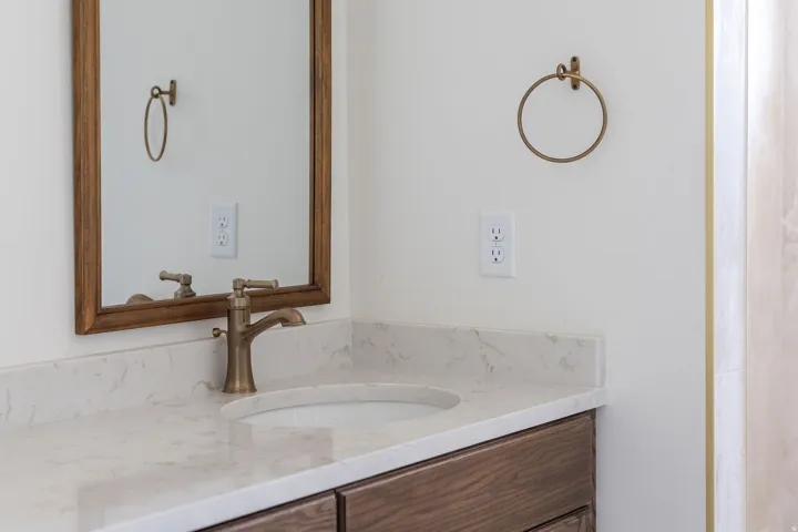 Wood-framed mirror, undermount sink, quartz countertop, and brushed brass fixtures