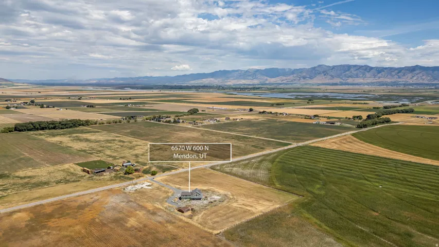 Single-family residence with an attached garage, situated on a substantial lot with an unpaved driveway, surrounded by agricultural fields, and framed by distant mountains
