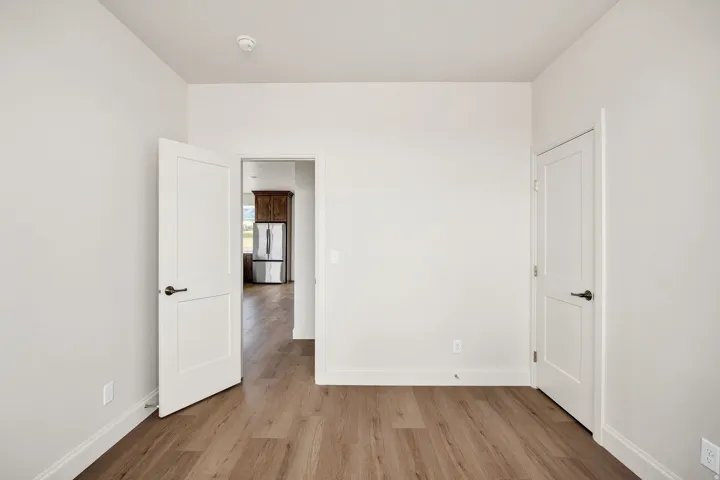 Wood-finish flooring with white baseboards, white interior doors with dark hardware, and light-colored walls