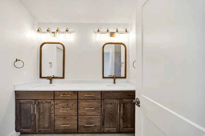 Dual vanity with a white countertop, undermount sinks, wood-finish cabinetry, and framed mirrors with brass hardware
