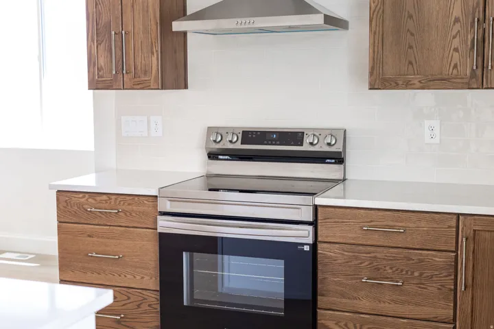 Stainless steel appliance suite featuring a range with an overhead vent hood, rich wood cabinetry, light-toned countertops, and a subway tile backsplash