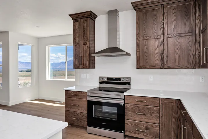 White countertops, stainless steel range, stainless steel range hood, dark wood-finish cabinetry, and light wood-finish flooring