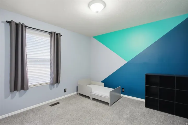 Recessed window with blinds, geometric accent wall, and wall-to-wall carpeting