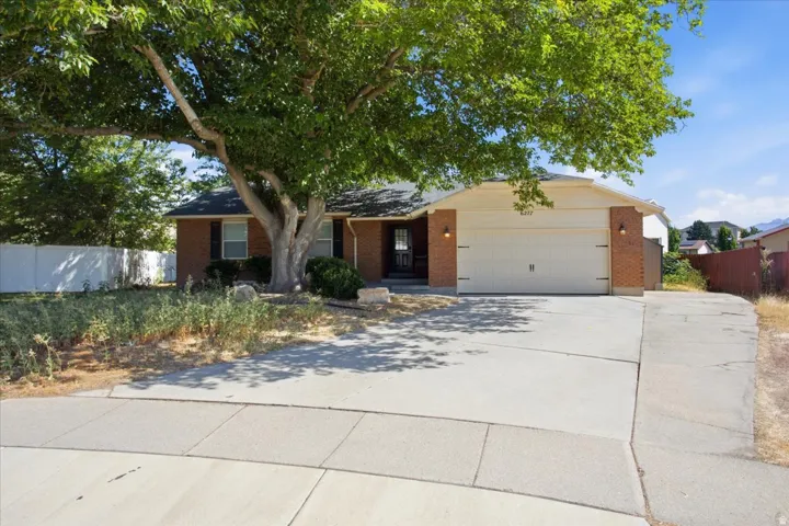Brick facade with contrasting dark shutters, two-car garage, mature front yard tree, and concrete driveway